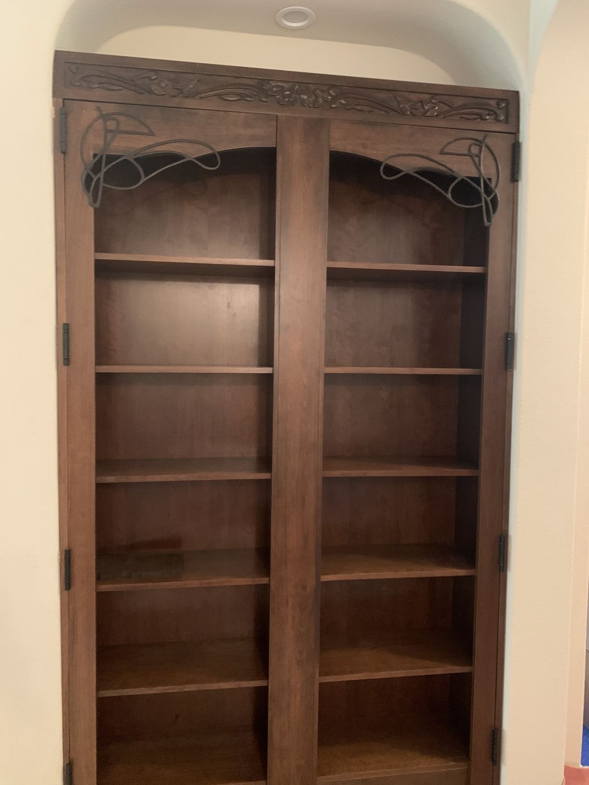 Arched built-in bookcase with a carved crown and iron scrollwork