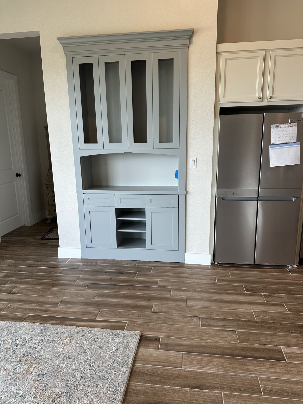 Grey built-in hutch with glass-front upper doors and open cubbies beside a kitchen