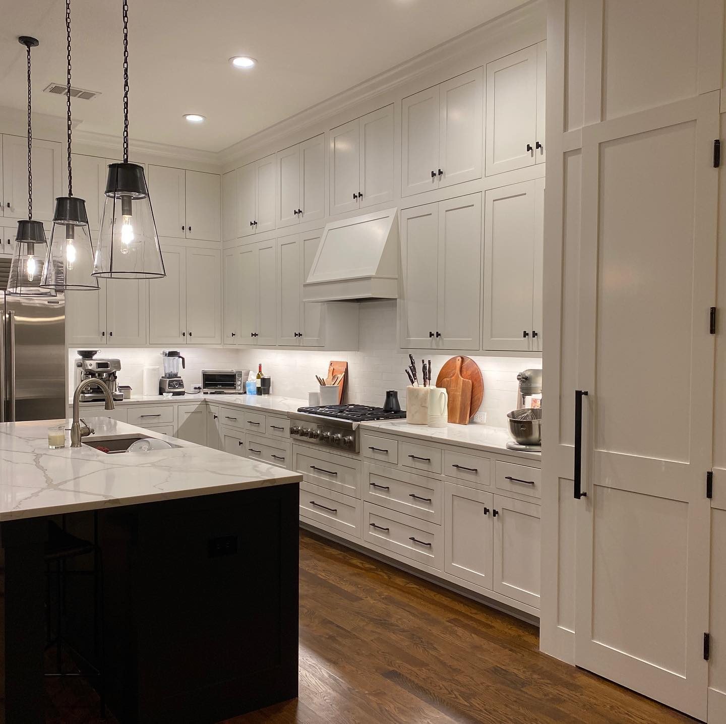 Bright painted shaker kitchen with full-height upper cabinets, a range hood and a dark island