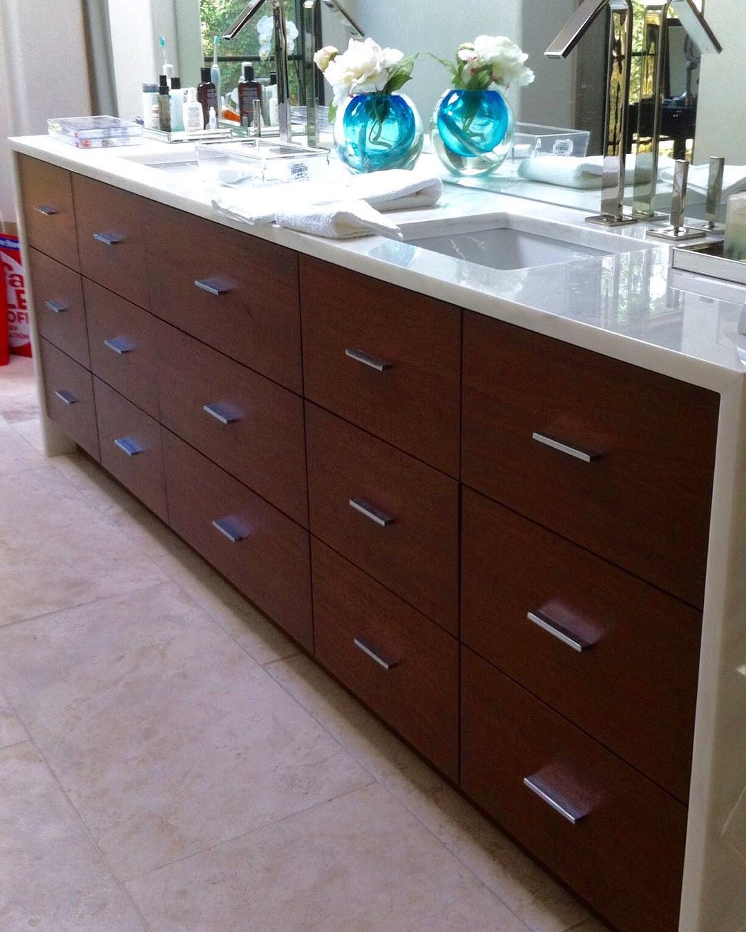 Long bathroom vanity with warm wood drawer fronts and a stone top