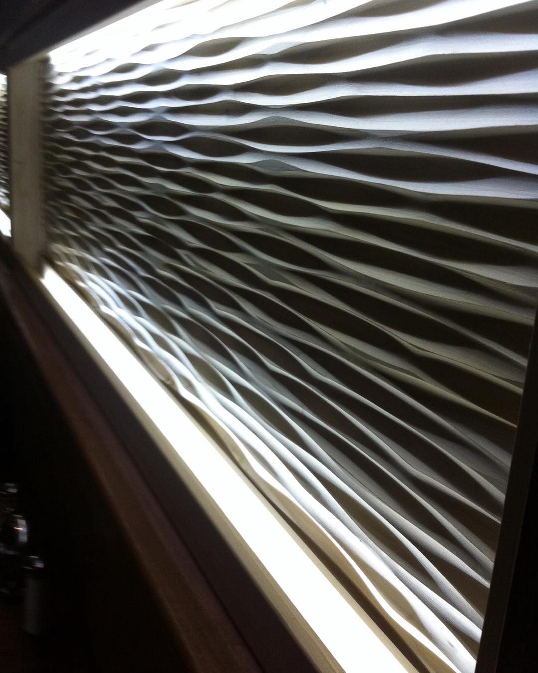 Carved wall panel with flowing wave shapes lit from the side